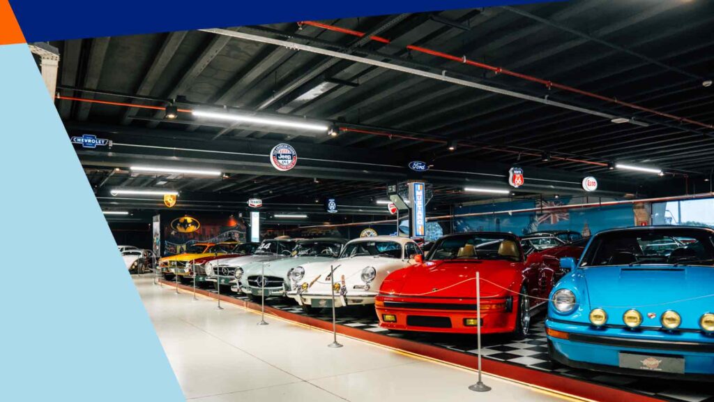 Museu de carros com exposição de clássicos esportivos e antigos, incluindo modelos Porsche e Mercedes em ambiente temático retrô.